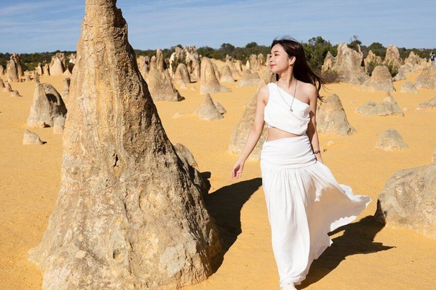 A person in white attire walking near a unique geological formation. 4