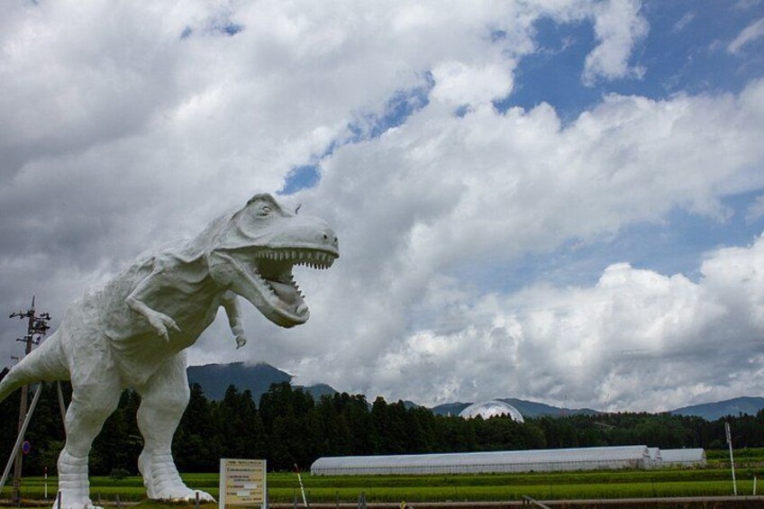 A large white dinosaur statue in a grassy field with a cloudy sky and mountains in the background. 5