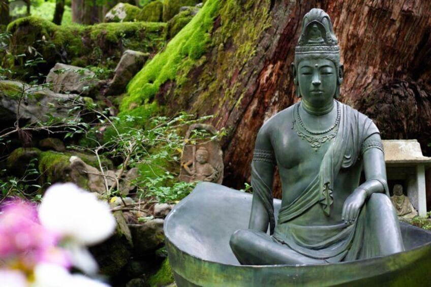 A seated statue in a natural setting with moss-covered rocks and a small pond. 4