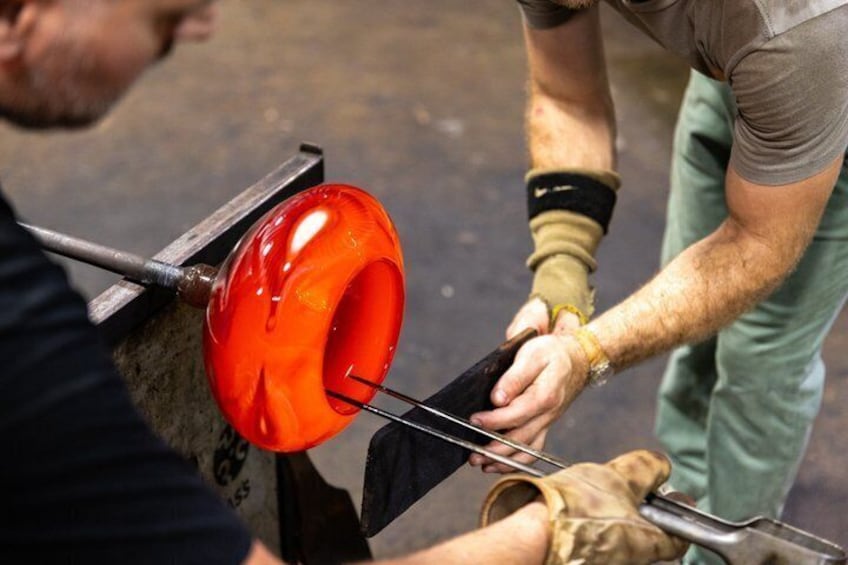A person working with a red glass object on a metal stand. 4