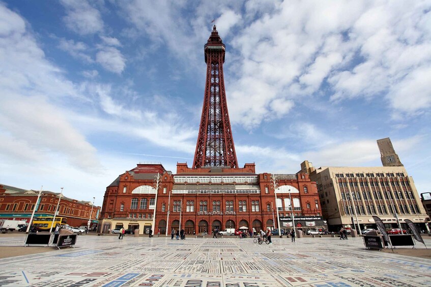 The Blackpool Tower, a red iron lattice tower, with a clear sky and a newspaper-covered plaza in the foreground. 1