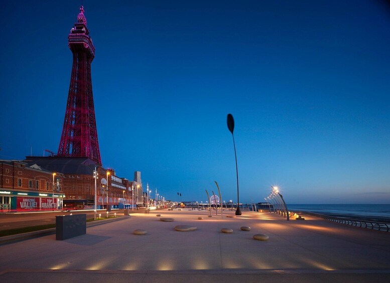 A coastal promenade at dusk with a prominent red-lit tower, a paved walkway, and a distant Ferris wheel. 5