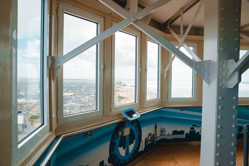 A room with large windows overlooking a cityscape, a mural with a blue anchor, and a metal truss structure. 2