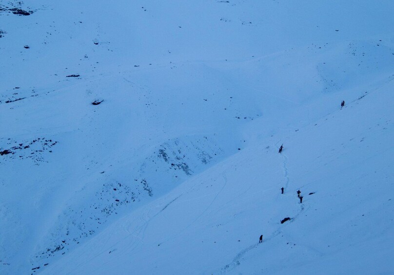 A snowy mountain slope with tracks and a few people walking. 5