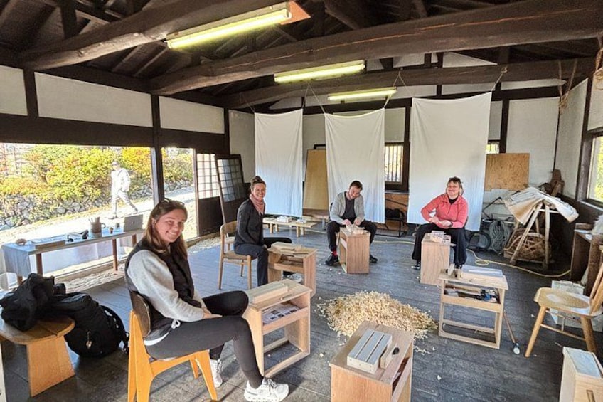 A group of people engaged in woodworking activities in a covered workshop with tables and tools. 1
