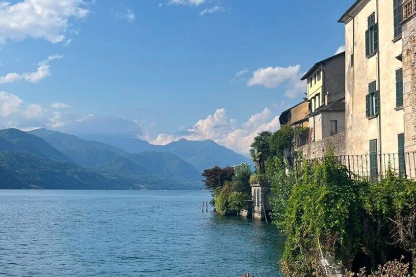 A calm lake with mountains in the background, a building with a balcony, and a clear sky. 1