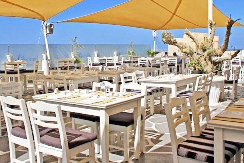 An outdoor dining area with white tables and chairs, yellow umbrellas, and a view of the sea. 3