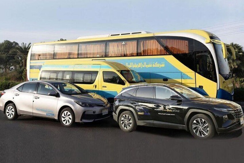 A yellow and blue bus with Arabic text, two cars parked in front, and a clear sky. 2