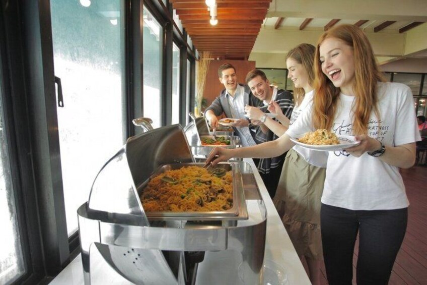 People serving themselves from a buffet table with a large dish of food. 2