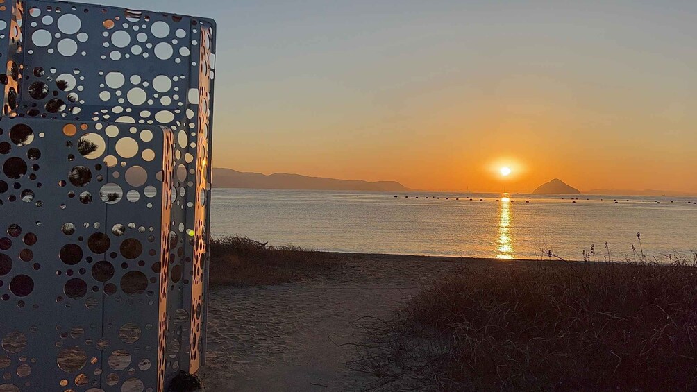 A sunset over a calm sea with a metal structure featuring circular cutouts. 2