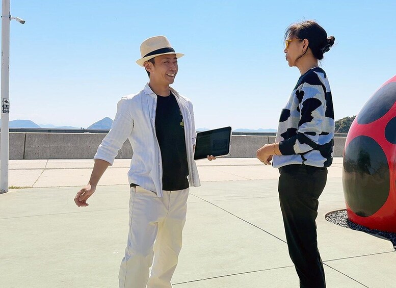 Two people walking on a rooftop with a large red and black spherical sculpture. 3