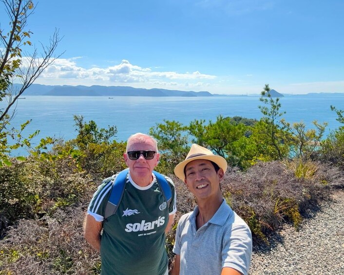 Two people standing on a rocky terrain with a view of a large body of water and distant mountains. 2