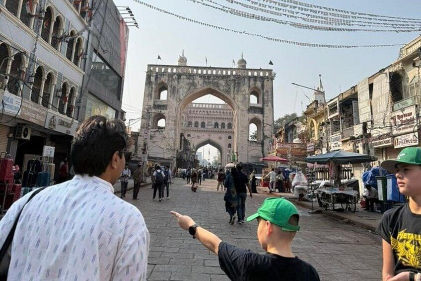An old stone archway with people walking around it. 1
