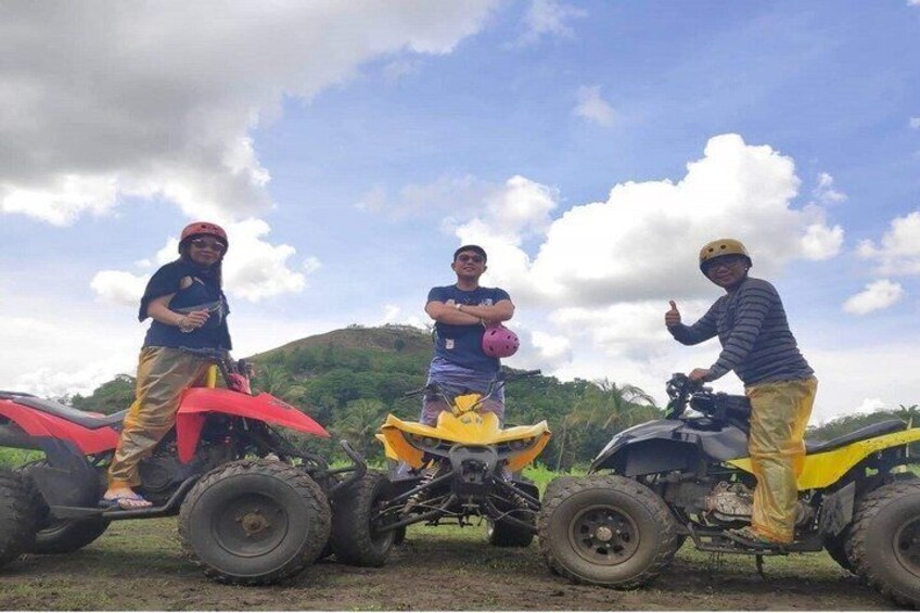 Three people standing next to off-road vehicles on a grassy field with hills in the background. 3