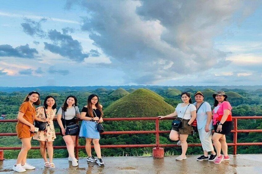 A group of people standing on a viewing platform with a scenic landscape in the background. 4