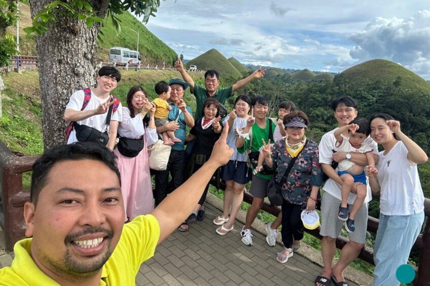 A group of people on a wooden boardwalk with a mountainous landscape in the background. 5