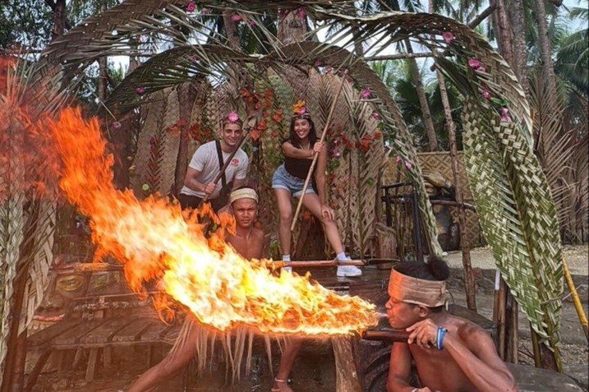 A fire with people around it, a wooden structure, and palm trees. 2