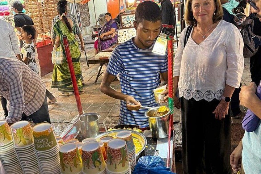 A street food vendor preparing food, with people and stalls in the background. 4