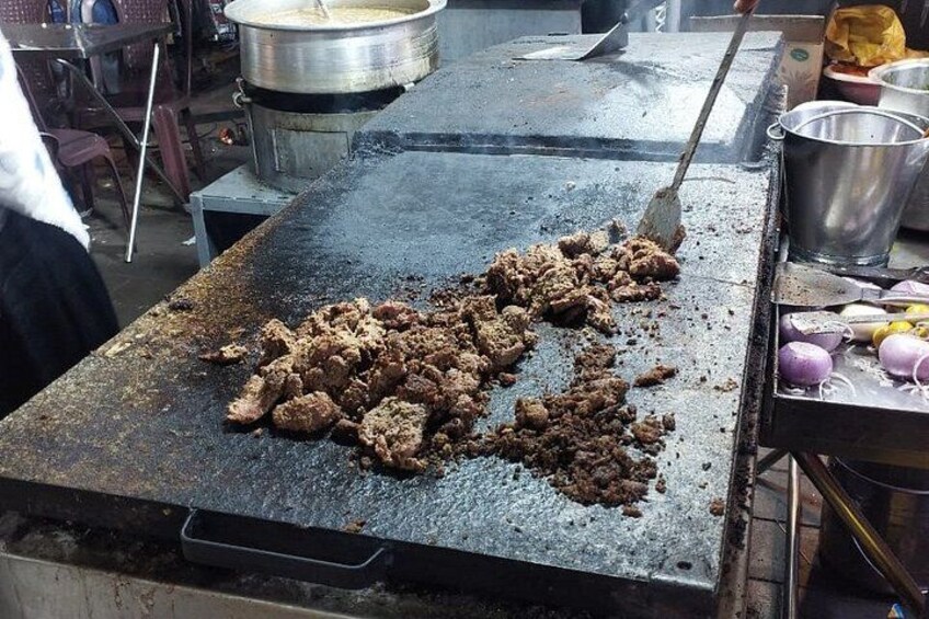 A cooking surface with meat being cooked, a pot in the background, and cooking utensils. 2