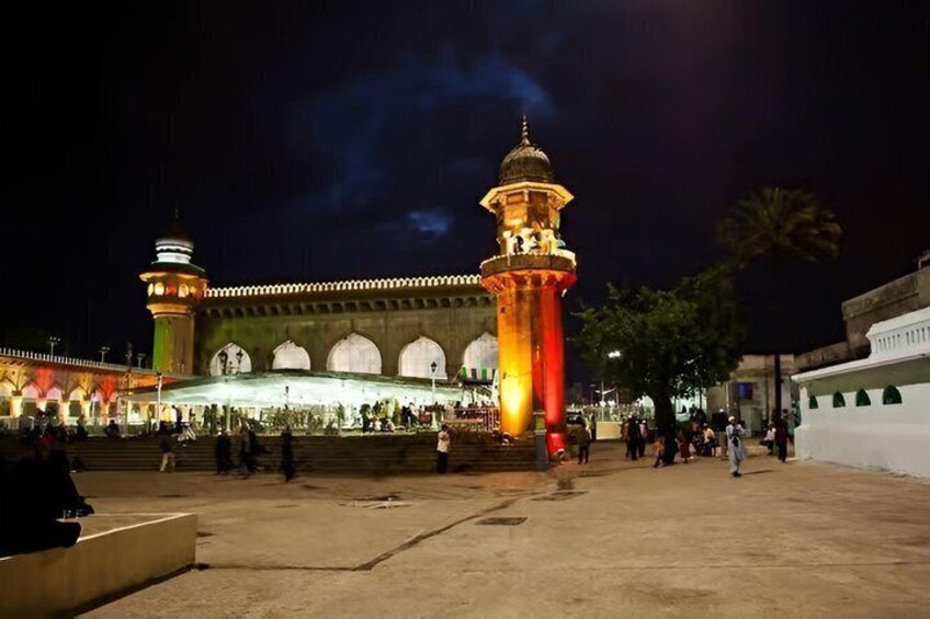 A mosque with a minaret, a courtyard, and people walking around. 4