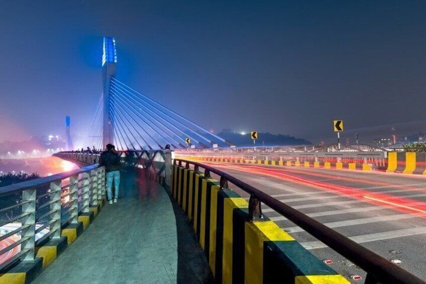 A bridge at night with illuminated cables, a pedestrian walkway, and road barriers. 5