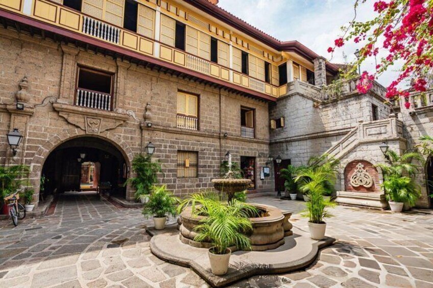 A courtyard with a fountain, potted plants, and a stone building with balconies. 5