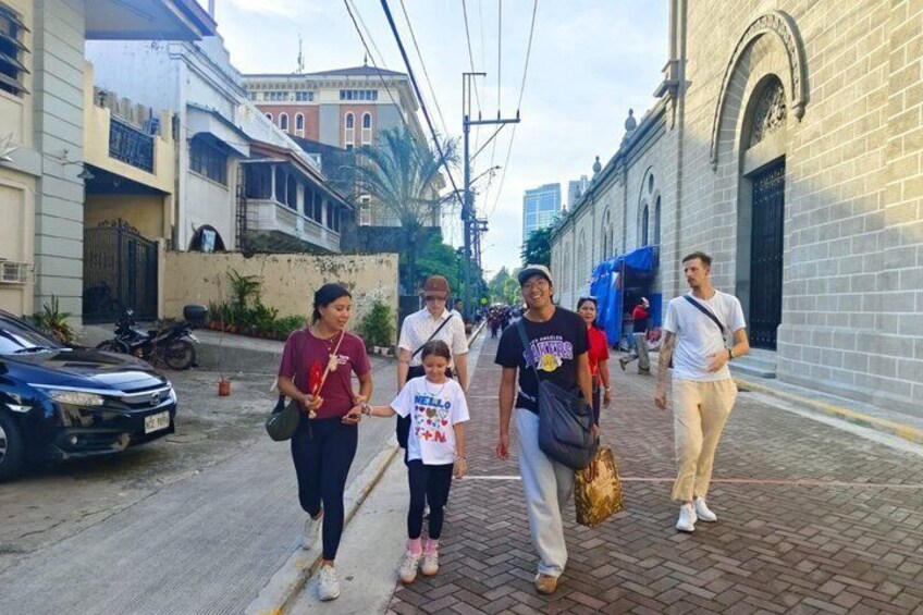 A group of people walking on a paved street with buildings and a parked car. 2