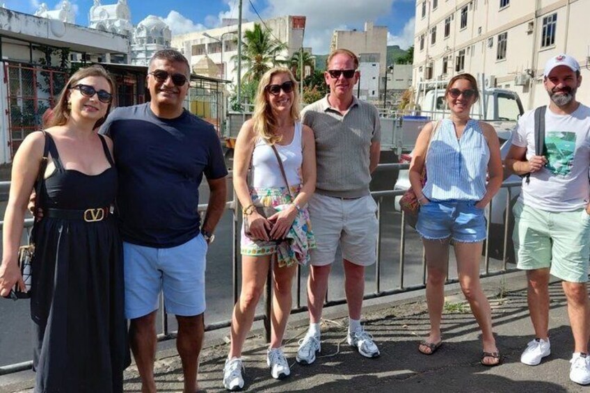 A group of people standing on a street with buildings and a clear sky in the background. 1