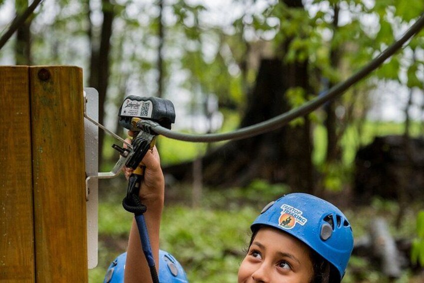 A person in a blue helmet using a power tool on a wooden structure in a forest. 2