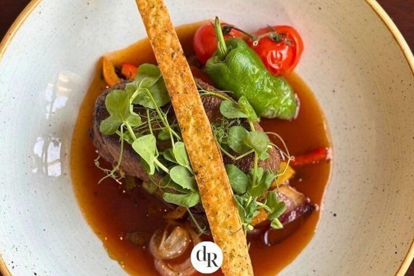 A dish with a piece of meat, greens, and a slice of bread on a plate. 2