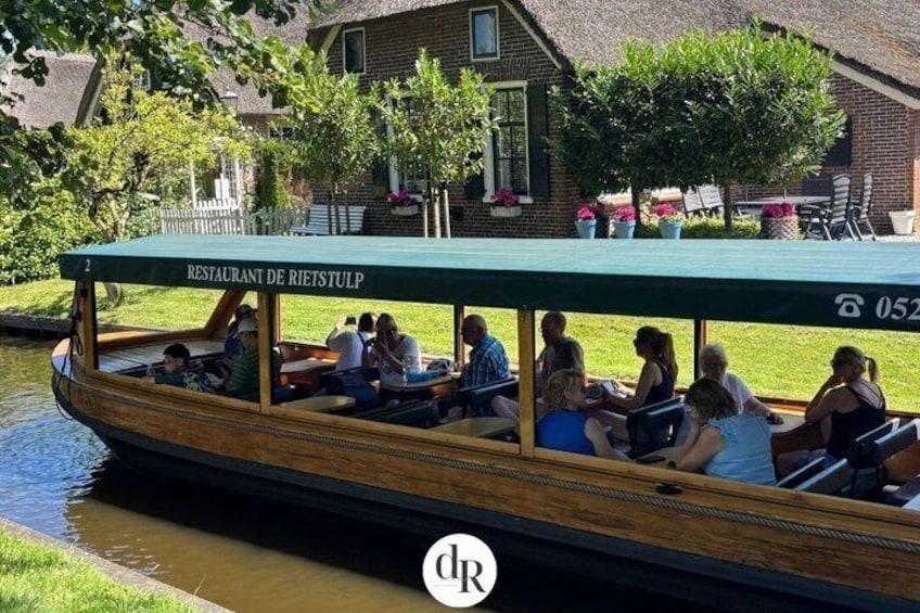 A boat with people on it, a river, and a building with a sign that says 'RESTAURANT DE RIESTULP' in the background. 1
