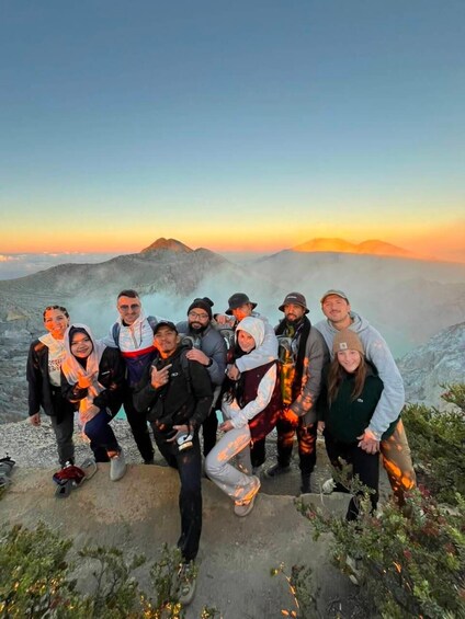 A group of people posing on a mountain ridge with a sunset in the background. 2