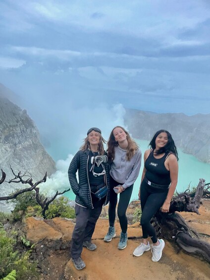 Three people standing on a rocky outcrop with a mountainous landscape and a turquoise lake in the background. 5