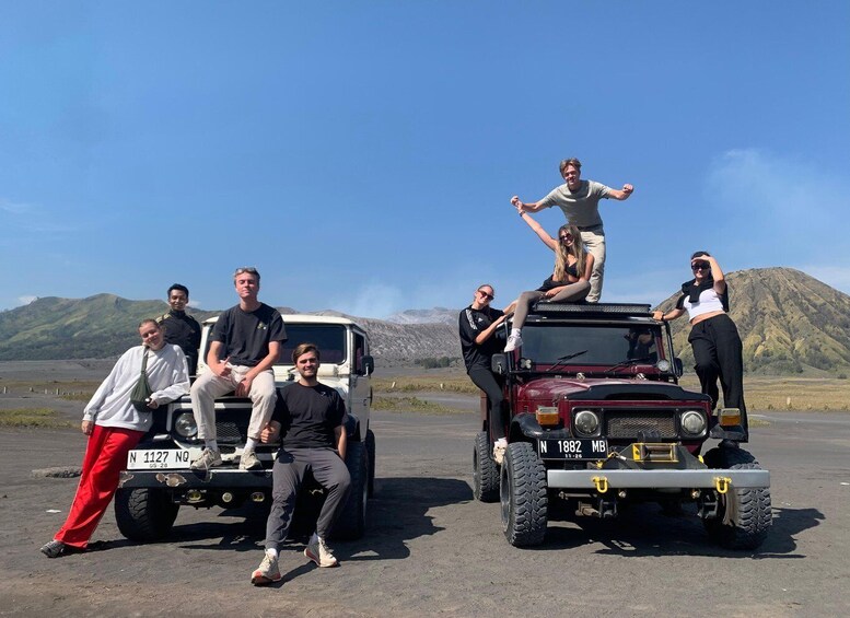 A group of people posing with two off-road vehicles in a barren landscape with mountains in the background. 1