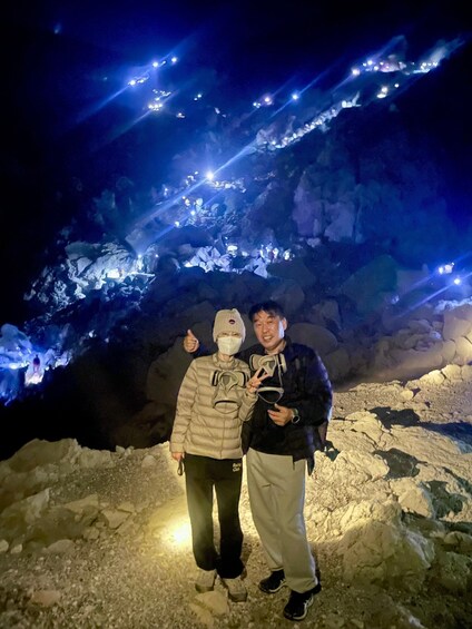 Two people standing in a cave with ice formations and lights. 4