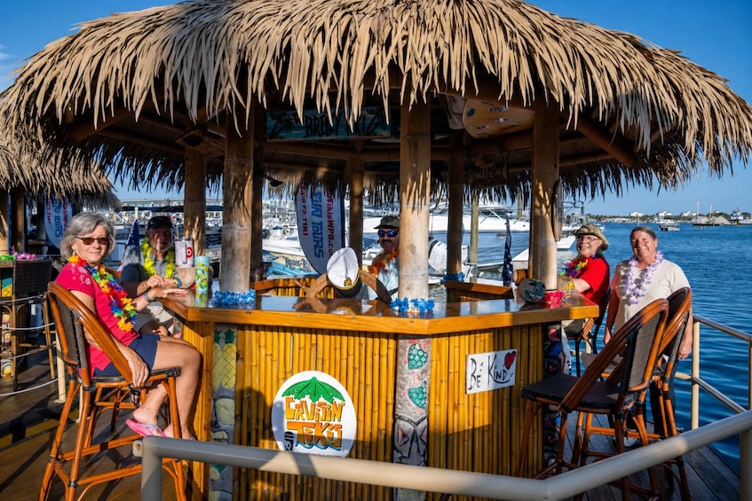 A thatched-roof bar on a boat with people sitting at tables, surrounded by water and boats in the background. 1