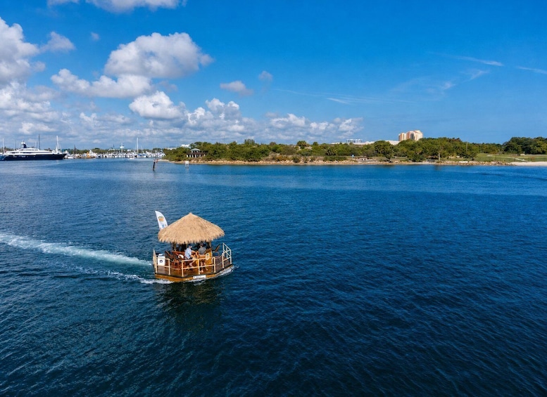 A boat with a thatched roof moving through a body of water, with a large ship and buildings on the shore in the background. 2