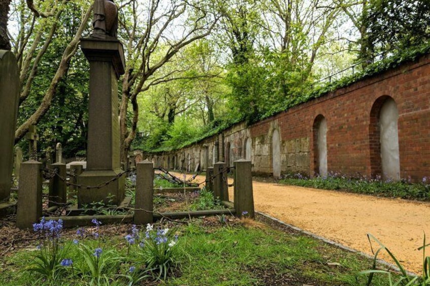 A cemetery with headstones, a brick wall, and a pathway. 2