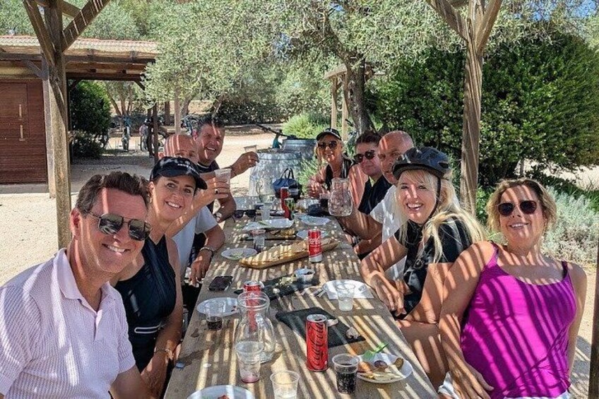A group of people seated at an outdoor dining table with drinks and food. 2