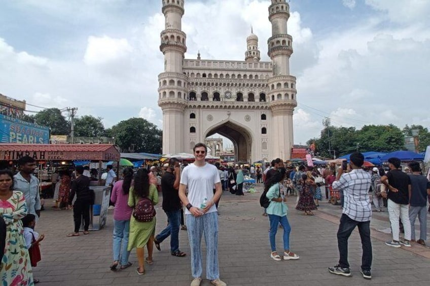 A large, historic building with multiple towers and an archway, surrounded by a busy market area with people and stalls. 5