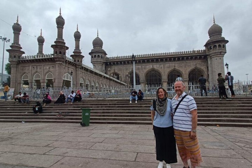 A historic building with multiple domes and minarets, a staircase leading up to it, and people sitting and standing around. 2