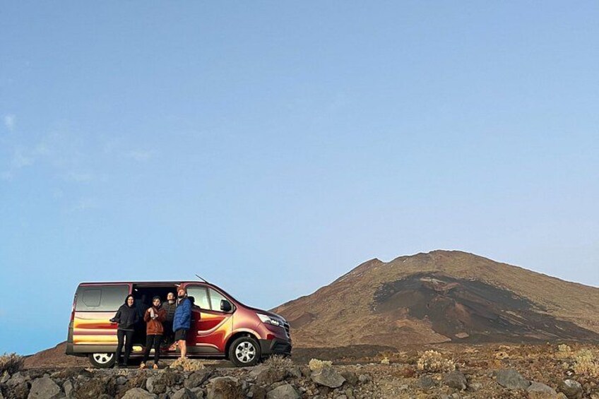 A red van parked on a rocky terrain with a mountain in the background. 3