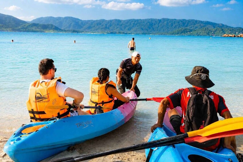 A group of people in a blue kayak on a calm lake with mountains in the background. 2