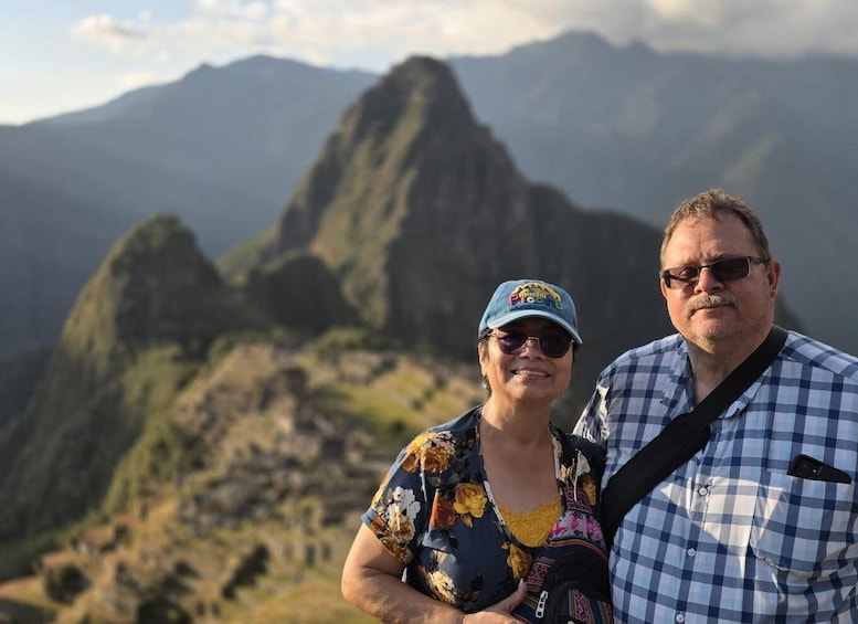 A person wearing a floral shirt and a cap, standing in front of a mountainous landscape. 3