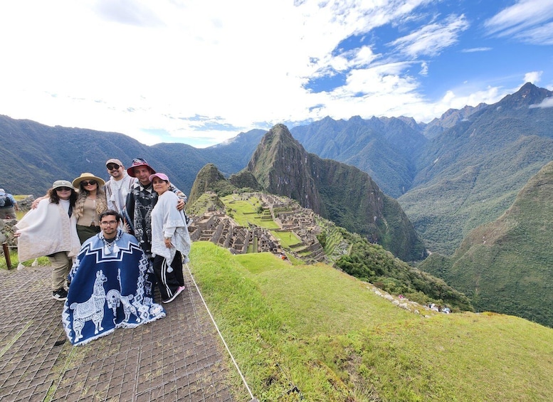 A group of people standing on a viewing platform at Machu Picchu, with the iconic Incan ruins and surrounding mountains in the background. 2