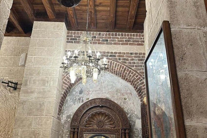 A stone archway with a chandelier, a framed picture, and a wooden ceiling. 2