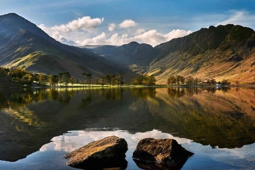 A calm lake with mountains in the background and two large rocks in the foreground. 5