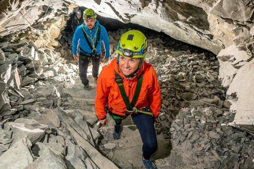 A person in an orange jacket and green helmet climbing rocky terrain. 3