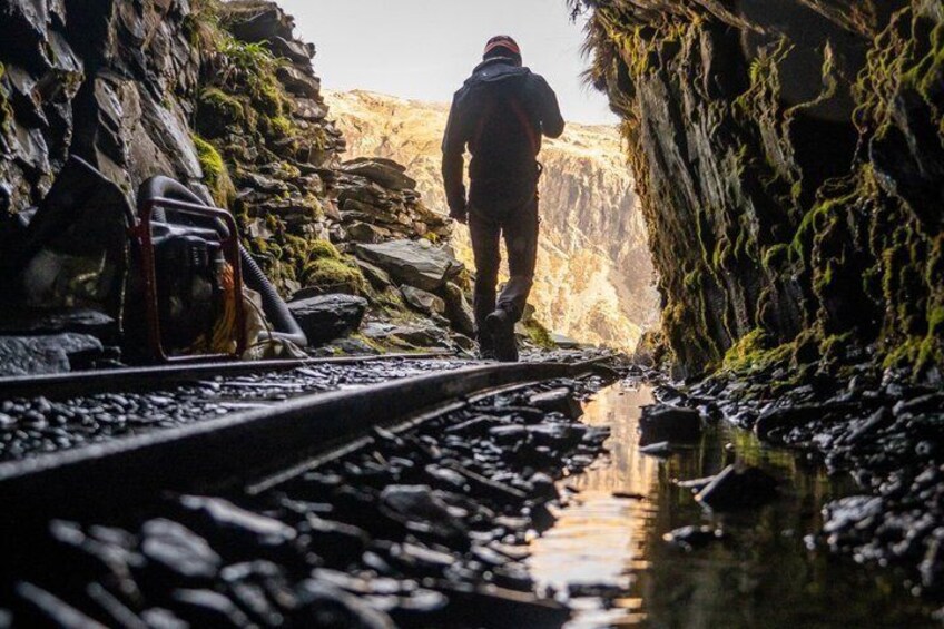 A person walking on a narrow path between rocky cliffs with a backpack and a bag. 2