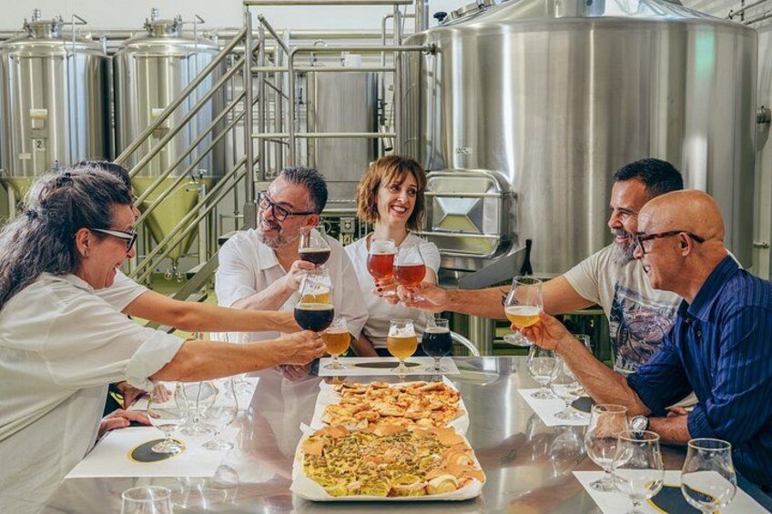 A group of people toasting with drinks around a table with a pizza. 3